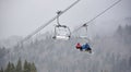 Bukovel, Ukraine - December 09, 2018: family skiers carrying up on cable chairlift over coniferous forest in dense fog