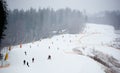 Bukovel, Ukraine - December 09, 2018: people skiing and snowboarding on ski run with snow cannon along slope in snowfall