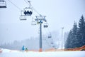 Bukovel, Ukraine - December 09, 2018: two skiers standing on slope under tall chairlift carrying people up in winter fog