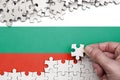 Bulgaria flag is depicted on a table on which the human hand folds a puzzle of white color