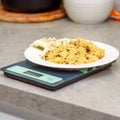 Bulgur, white fish and vegetables on a kitchen scale. Delicious healthy warm salad on a marble table.Counting calories.