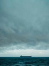 A bulk carrier ship passing under heavy rain clouds and storm clouds and rough weather Royalty Free Stock Photo