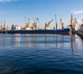 Bulk carrier ship in the port on loading. Bulk cargo ship under port crane bridge. Ship in seaport at sunset Royalty Free Stock Photo