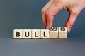 Bull or bulldozed symbol. Businessman turns wooden cubes and changes word Bull to Bulldozed. Beautiful grey table grey background