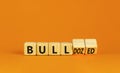 Bull or bulldozed symbol. Businessman turns wooden cubes and changes word Bull to Bulldozed. Beautiful orange table orange