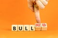 Bull or bulldozed symbol. Businessman turns wooden cubes and changes word Bull to Bulldozed. Beautiful orange table orange