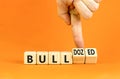 Bull or bulldozed symbol. Businessman turns wooden cubes and changes word Bull to Bulldozed. Beautiful orange table orange