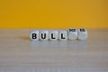 Bull or bulldozed symbol. Turned wooden cubes and changes word Bull to Bulldozed. Beautiful wooden table orange background.