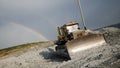 Bulldozer in background of open pit. Bulldozer stands motionless on background of natural phenomenon of rainbow in sky