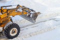 A bulldozer with a bucket clears snow from the road in winter after a snowfall Royalty Free Stock Photo