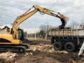 Bulldozer clearing land from old bricks and concrete from walls with dirt and trash. Backhoe machinery ruining house. Excavator