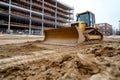 Bulldozer at a construction site clearing soil, with a building under construction in the background. Royalty Free Stock Photo