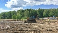 Bulldozer and excavator working on a muddy construction site near a forest under a cloudy blue sky, representing land development Royalty Free Stock Photo