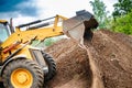 A bulldozer or a loader is actively digging dirt in a vast field, moving and reshaping the earth