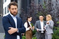 Bullying at work. Upset man standing outside office center with hands folded and head bowed, women and men team laughing Royalty Free Stock Photo