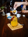 Hand pouring coffee into glass with orange juice and ice cubes at wooden table, selective focus, cold Iced glass of espresso with Royalty Free Stock Photo