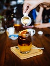 Hand pouring coffee into glass with orange juice and ice cubes at wooden table, selective focus, cold Iced glass of espresso with Royalty Free Stock Photo