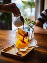 Hand pouring coffee into glass with orange juice and ice cubes at wooden table, selective focus, cold Iced glass of espresso with Royalty Free Stock Photo