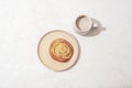 Bun on a plate and coffee with milk on a white table. Breakfast concept, harsh shadows. Top view, flat lay Royalty Free Stock Photo