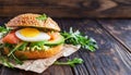 Burger with salmon, avocado, egg, rucola on dark wooden background. Delicious fast food