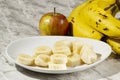 A bunch of bananas, a sliced banana, and an apple on a plate on a table. Selective focus Royalty Free Stock Photo