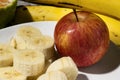 A bunch of bananas, a sliced banana, and an apple on a plate on a table. Selective focus Royalty Free Stock Photo