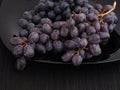 Bunch of blue Sultana grapes on a black plate. Grapes is unwashed