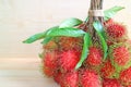 Bunch of Bright Color Red and Green Fresh Ripe Rambutan Fruits with Leaves Isolated on Wooden Table