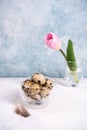 A bunch of brown quail eggs in a transparent bowl. Nearby are pink tulip. White and blue pastel background. Vertical oriented Royalty Free Stock Photo