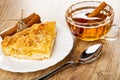Bunch of cinnamon sticks, piece of lemon pie in plate, cup of tea, spoon on wooden table