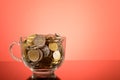 Bunch of coins in a glass cup on the table over red background Royalty Free Stock Photo