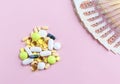 A bunch of colorful pills and Russian bills on a pink background. The cost of treatment and health concept