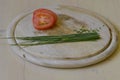 A bunch of fresh chives and slices of tomato on wooden chopping board