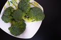 Bunch of fresh green broccoli on white plate over black wooden background. Healthy food. Diet food Royalty Free Stock Photo