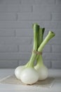 Bunch of fresh green spring onions on white wooden table against brick wall, closeup Royalty Free Stock Photo