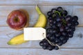 Bunch of fresh organic black grapes, banana, red apple, and a blank label tag on a wooden table Royalty Free Stock Photo