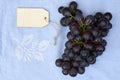 Bunch of fresh organic black grapes on a vintage tea towel, and a blank label tag on a wooden table Royalty Free Stock Photo