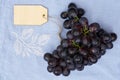 Bunch of fresh organic black grapes on a vintage tea towel, and a blank label tag on a wooden table Royalty Free Stock Photo