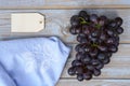 Bunch of fresh organic black grapes, a vintage tea towel, and a blank label tag on a wooden table Royalty Free Stock Photo