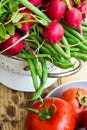 Bunch of fresh organic green beans, red radish in metal colander, ripe tomatoes on wood kitchen table, healthy diet, clean eating, Royalty Free Stock Photo