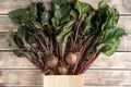 Bunch of fresh ripe beets with long green haulm on faded wooden table, top view. Unpacking beetroots from eco paper bag