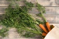 Bunch of fresh ripe carrots with long green haulm on faded wooden table, top view. Unpacking vegetables from eco paper