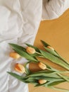 Bunch of fresh yellow tulips lies on a bed with a white blanket and yellow sheet. Top view. Cozy home at morning.