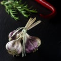 A bunch of garlic on a black background next to the rormarin and chili peppers Royalty Free Stock Photo