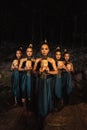 A Bunch of girls in green costumes holding a wooden masks in their hands while standing between the big rocks in front of the