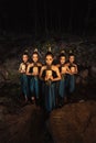 A Bunch of girls in green costumes holding a wooden masks in their hands while standing between the big rocks in front of the