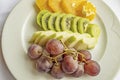 Bunch of grapes, sliced kiwi, apple and orange fruits in white plate Royalty Free Stock Photo