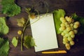 Bunch of green grapes with leaves, notebook and pen on the wooden background Royalty Free Stock Photo