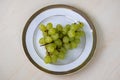 A bunch of green grapes on a white plate. Top view of fresh grape fruits on wooden background Royalty Free Stock Photo