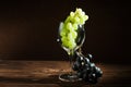 A bunch of green grapes and a wine glass on a dark background in the conditions of artificial hard lighting close up. In a glass o